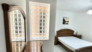 Une chambre à coucher avec un lit en bois, une table de chevet, un miroir et une fenêtre ornée de vitraux.