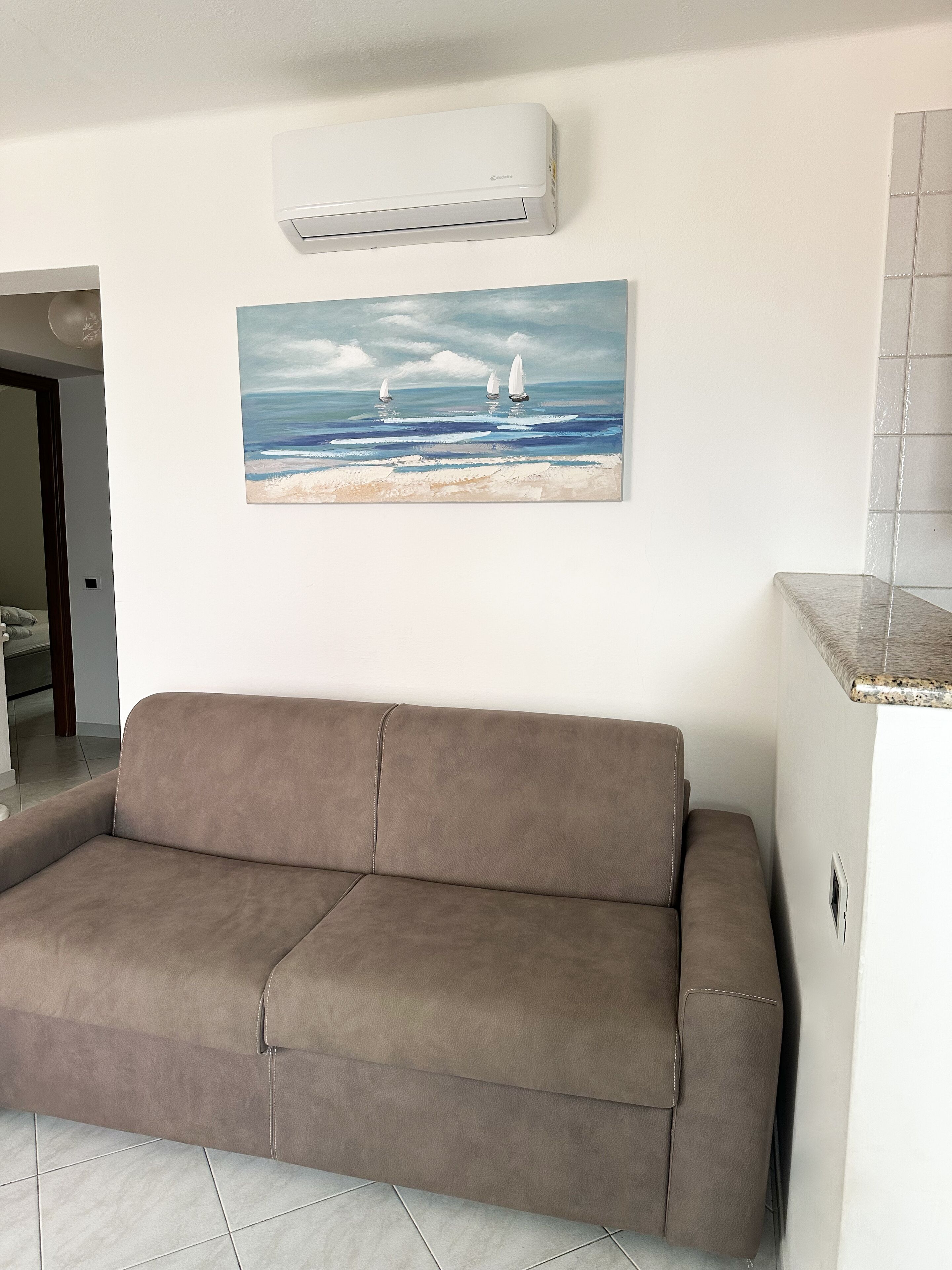 Ein Wohnzimmer mit einem braunen Sofa, einem Gemälde von Segelbooten auf dem Meer und einer Klimaanlage an der Wand.