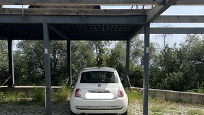 Une voiture blanche était garée sous un abri de stationnement doté d’un toit en métal et de piliers en béton.