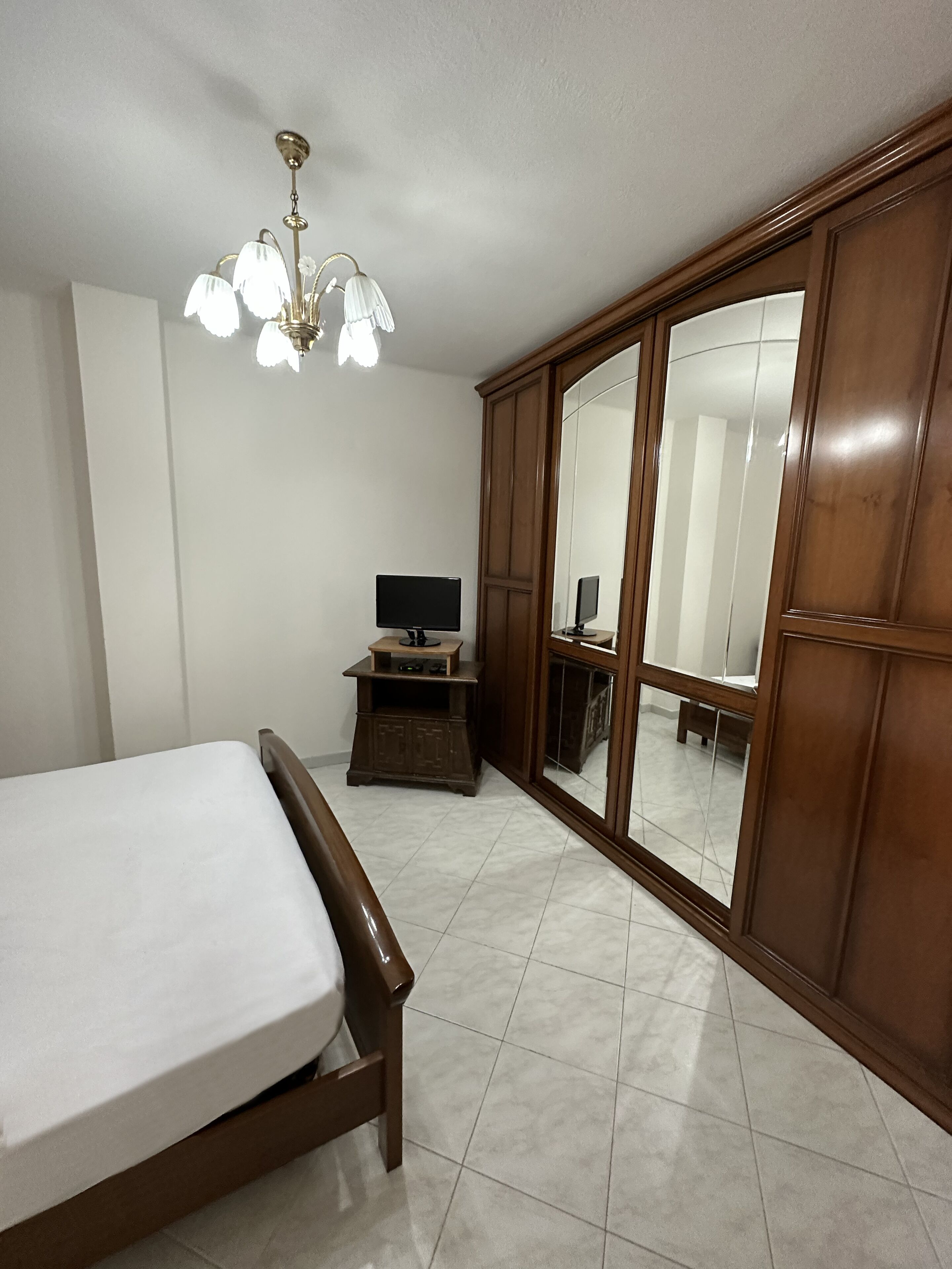 A bedroom with a bed, a television on a stand, a wardrobe, and a chandelier.