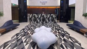 A modern lobby with a geometric patterned floor, a reception desk, and a large illuminated sign reading "ALLIANCE PALACE". - Dream Apartments Batumi (Batumi)