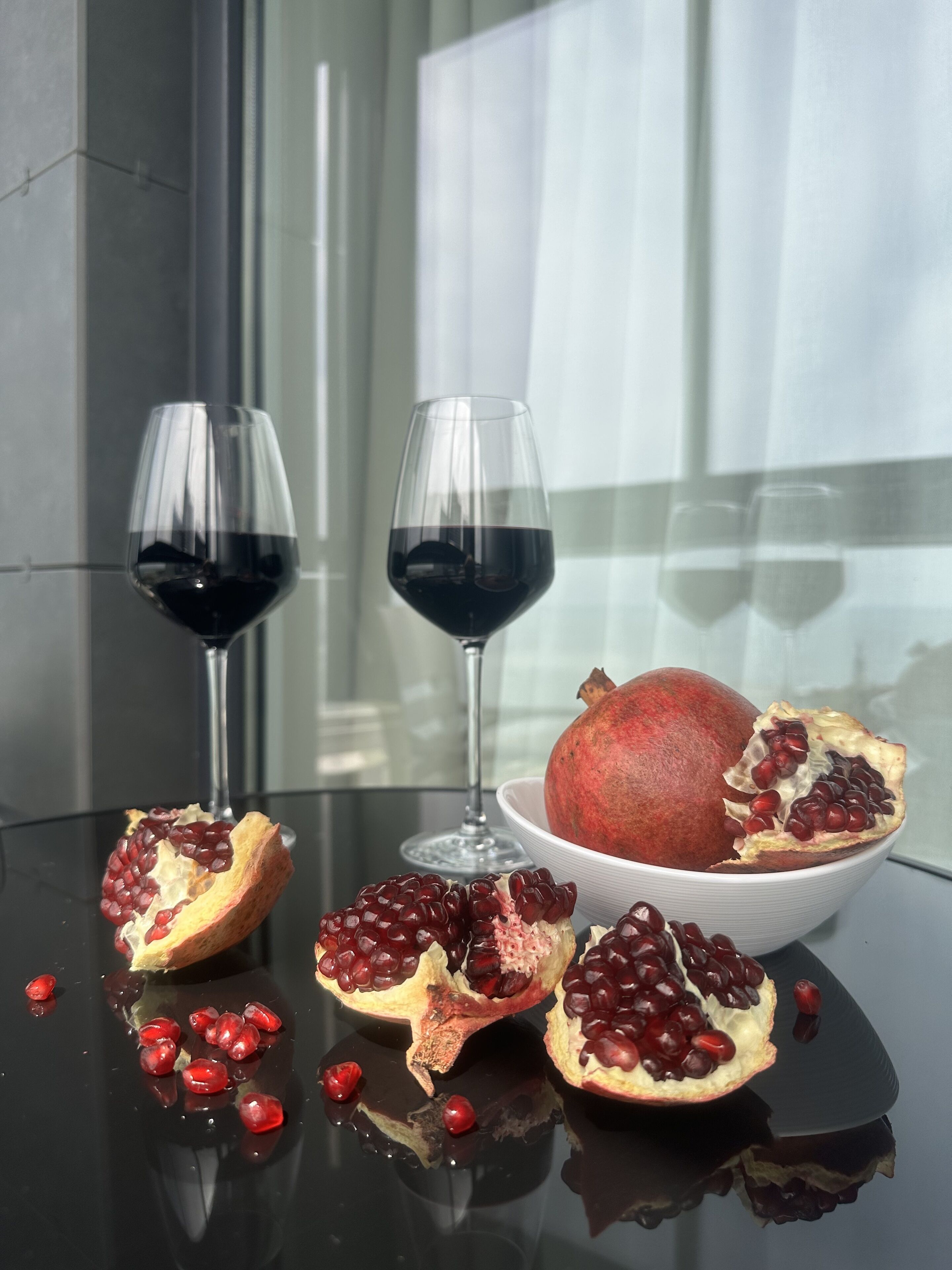 A table with two wine glasses, a bowl of pomegranate, and a pomegranate cut in half.