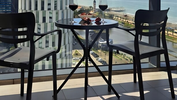 A balcony with a table and chairs, overlooking a cityscape and the sea. - Dream Apartments Batumi (Batumi)