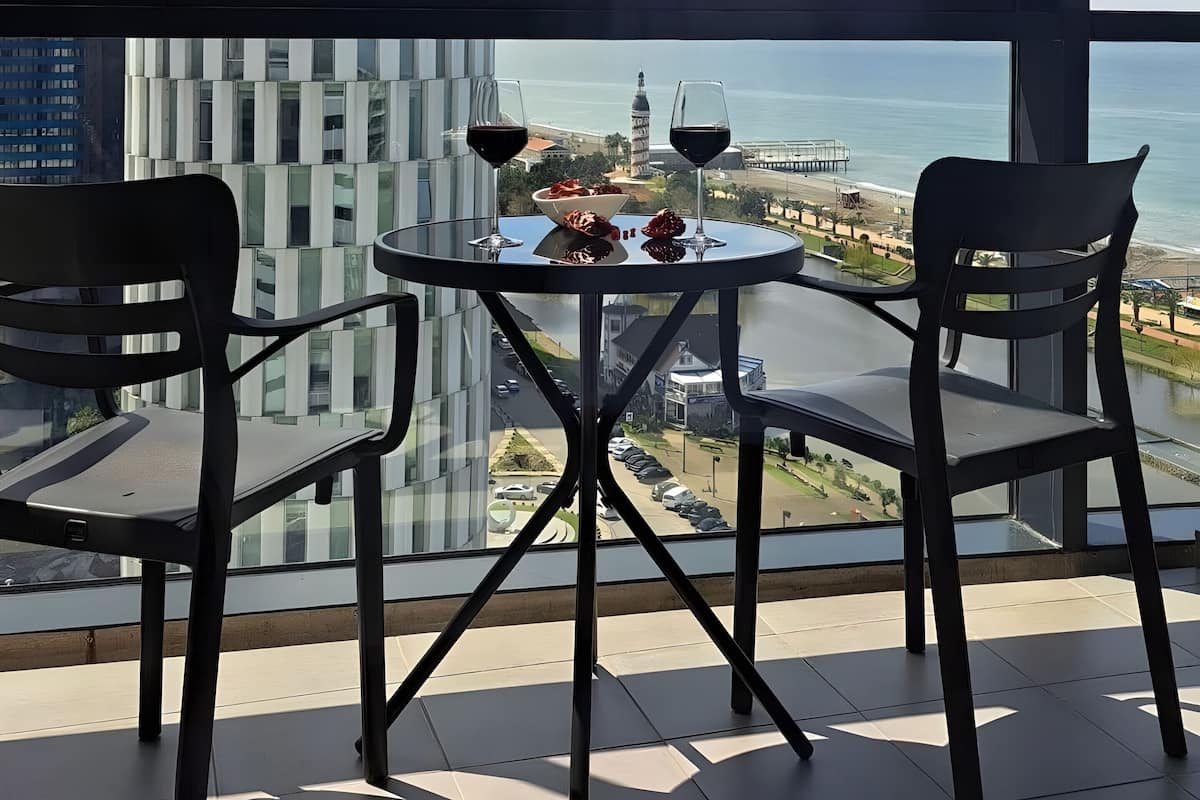 Un balcon avec une table et des chaises, offrant une vue sur le paysage urbain et la mer.