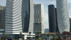 A modern building with a curved facade and a large central window, surrounded by other high-rise buildings and a body of water. - Dream Apartments Batumi (Batumi)