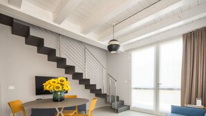 Un salon moderne avec un escalier, un coin repas avec des chaises jaunes et un canapé agrémenté de coussins jaunes.