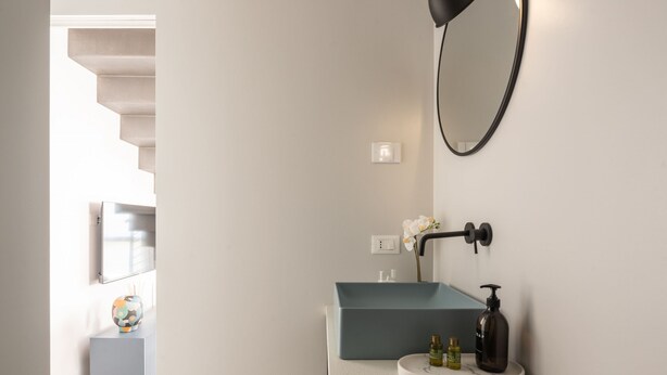 Une salle de bain moderne avec un lavabo rectangulaire, un miroir rond et un luminaire suspendu noir.