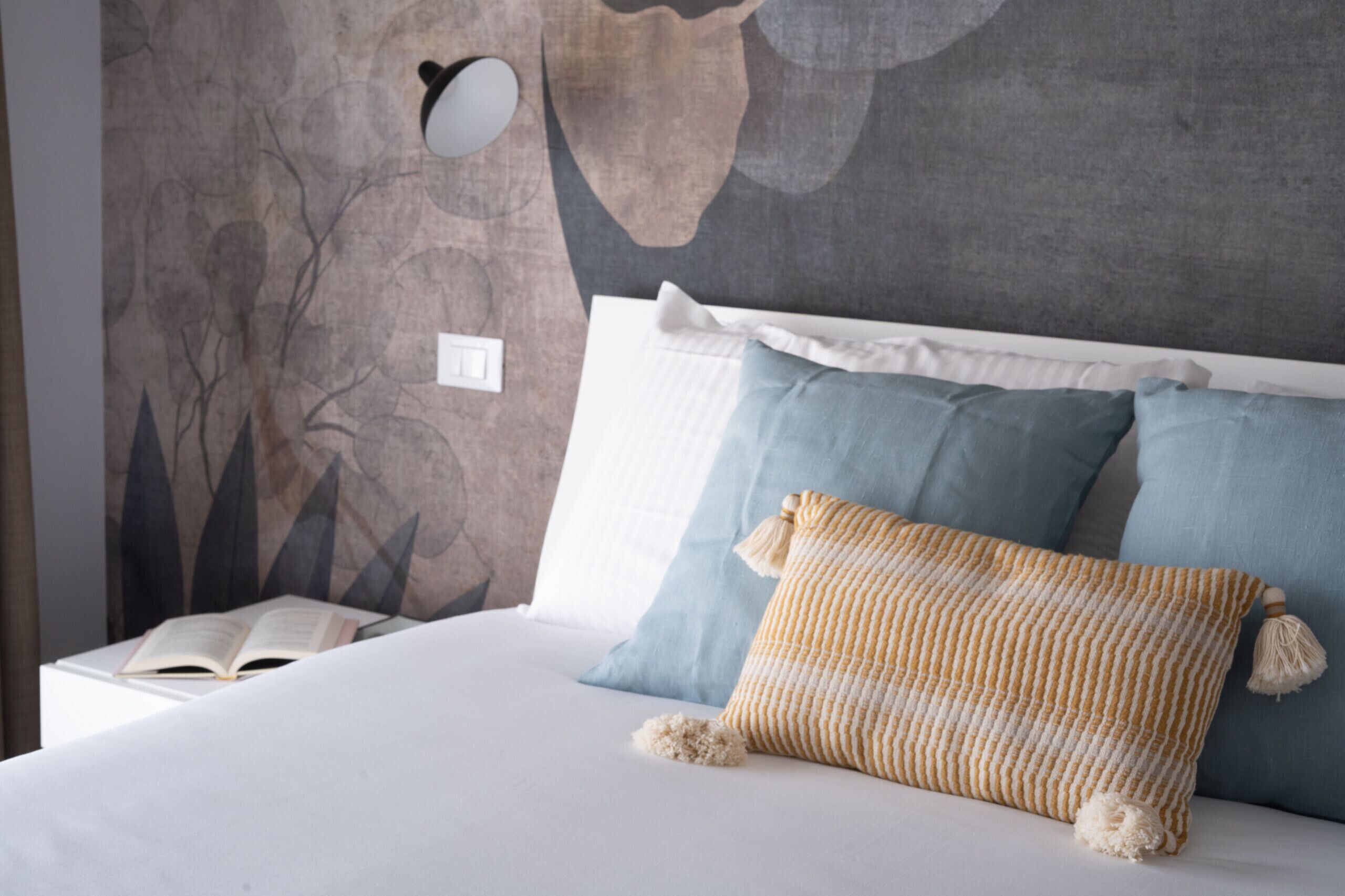 Cama arrumada com lençóis brancos e várias almofadas, incluindo uma almofada listrada amarela e branca.