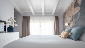 Une chambre à coucher avec un grand lit, un téléviseur posé sur une commode blanche et un luminaire fixé au mur.