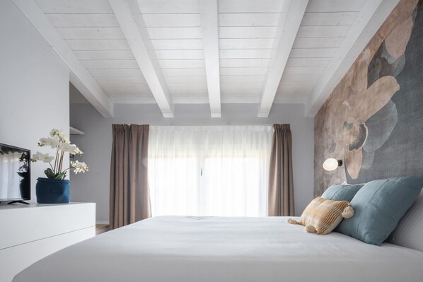 A bedroom with a large bed, a TV on a white dresser, and a wall-mounted light fixture.