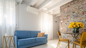 Une pièce avec un canapé bleu, une petite table ronde entourée de chaises jaunes et un mur orné d’un motif floral.