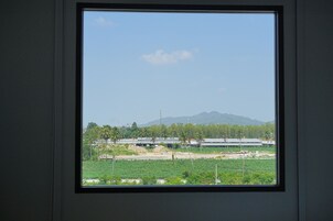 Una ventana con vista a una obra, vegetación y montañas distantes.