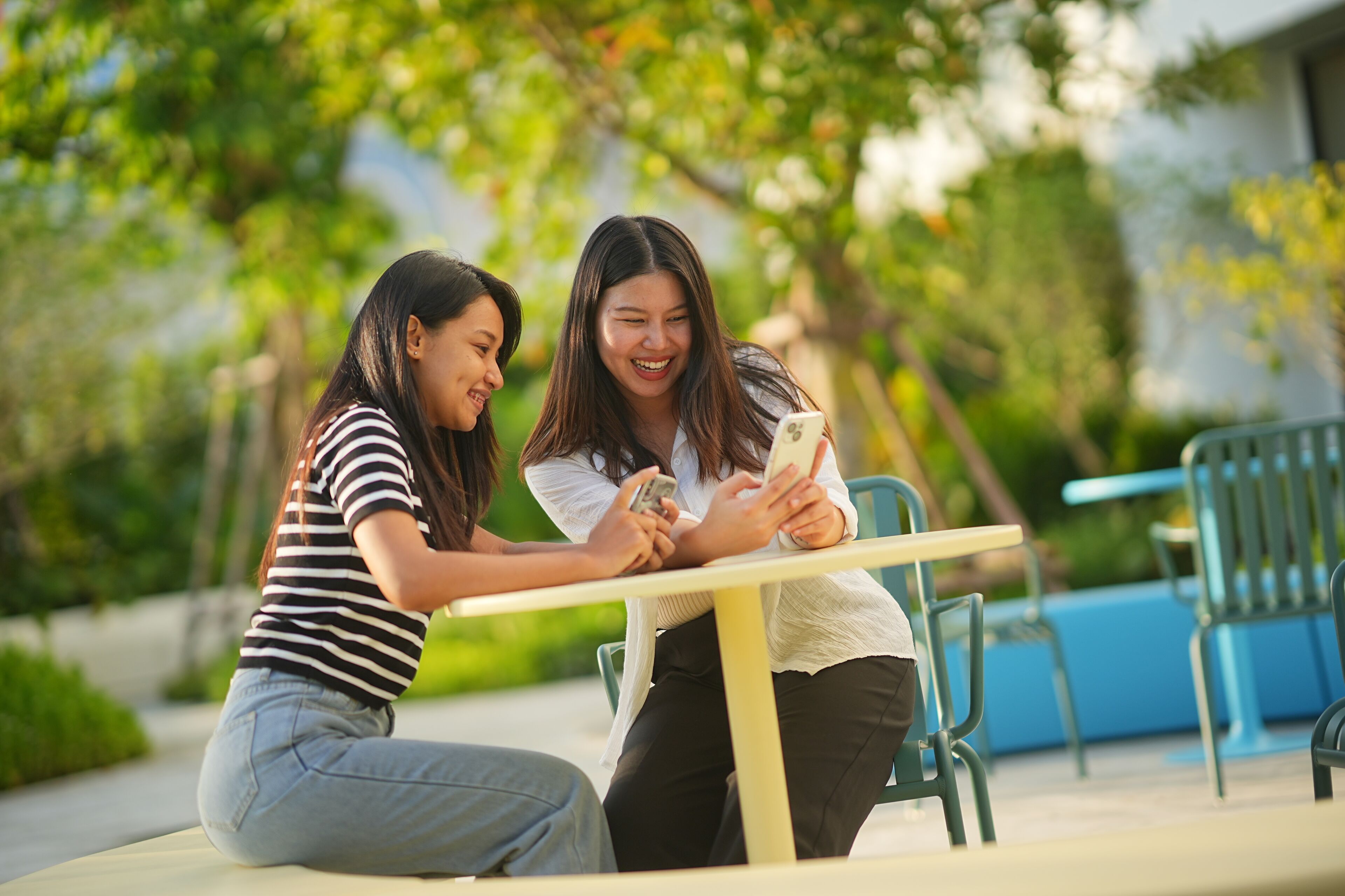 Two people sitting at a table outdoors, using smartphones.
