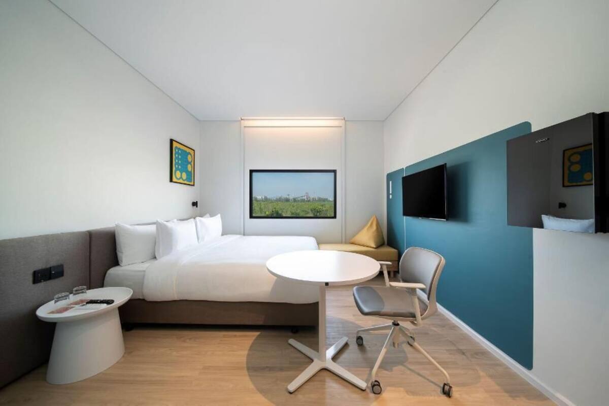 Une chambre d’hôtel moderne, équipée d’un lit, d’une table ronde, d’une chaise, d’un téléviseur fixé au mur et d’une fenêtre donnant sur un beau paysage.