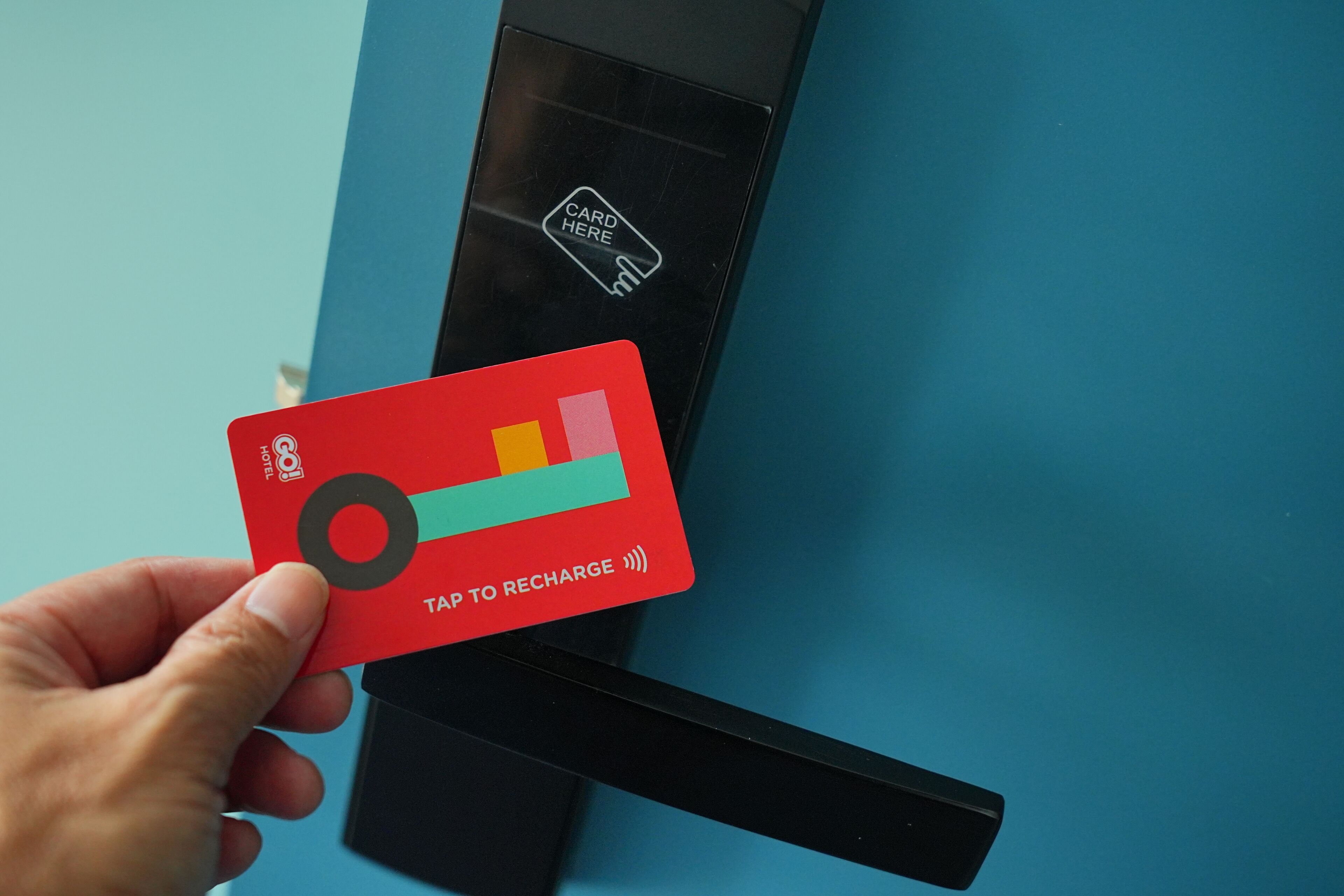 A hand holding a red card with a tap to recharge symbol, placed on a blue surface with a card reader.