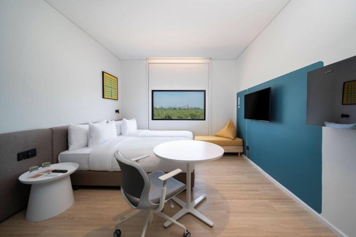 Une chambre d’hôtel moderne équipée d’un lit, d’un canapé, d’une petite table, d’une chaise, d’un téléviseur et d’une grande fenêtre donnant sur la ville.