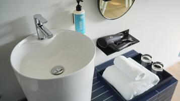 Un baño con un lavamanos blanco, un dispensador de jabón, un secador de pelo y un perchero para toallas.