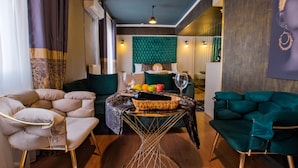 Una sala moderna con un sofá tapizado color turquesa, un sillón color beige y una mesa de centro de vidrio con frutas y copas de vino.