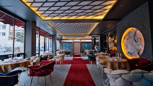 Un interior de restaurante moderno con alfombra roja, mesas, sillas y un diseño de techo único.