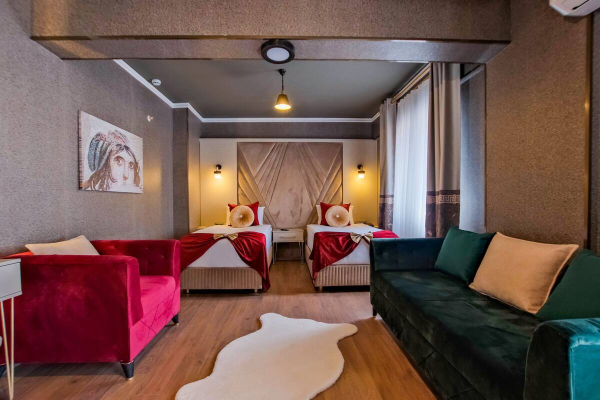 A hotel room with two beds, a red sofa, a green sofa, a white rug, and a painting on the wall.