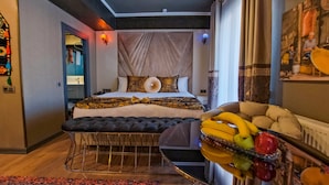 Un hotel moderno con una cama grande, una mesita redonda con fruta y vistas a la ciudad.