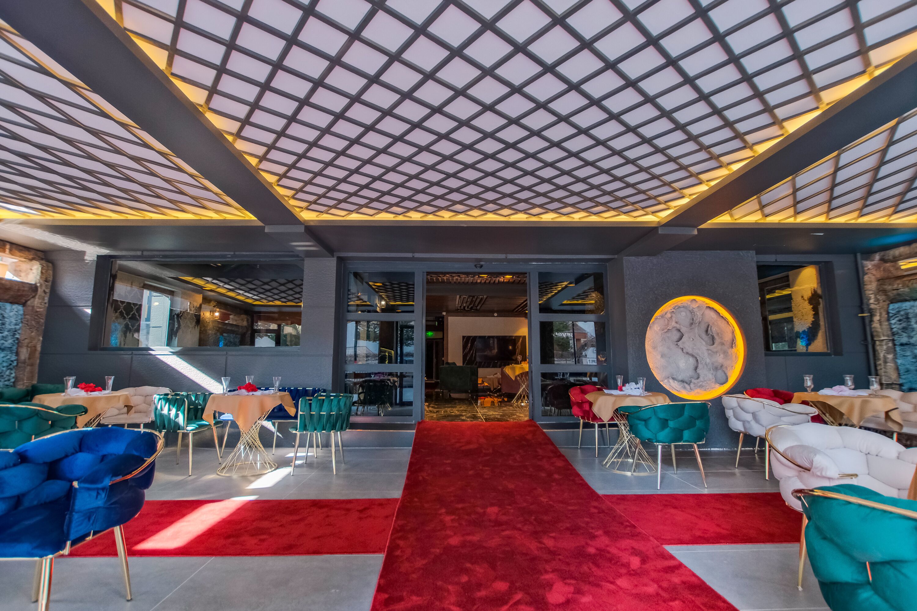 A modern restaurant interior with a red carpet, glass partitions, and a variety of seating options including chairs and sofas.
