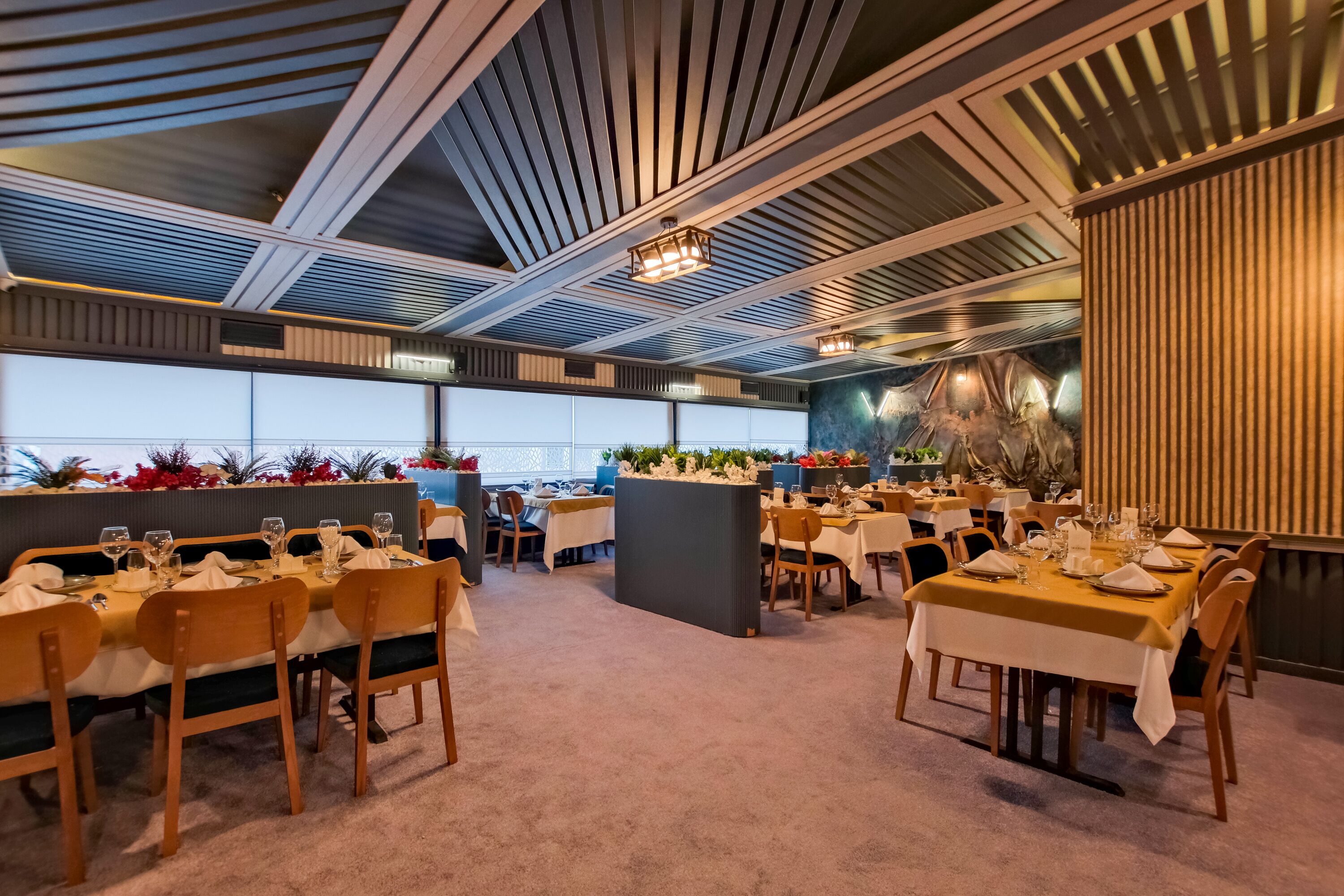 Un restaurante con varias mesas dispuestas para comer, que presenta un diseño moderno en el techo y vistas a la ciudad.