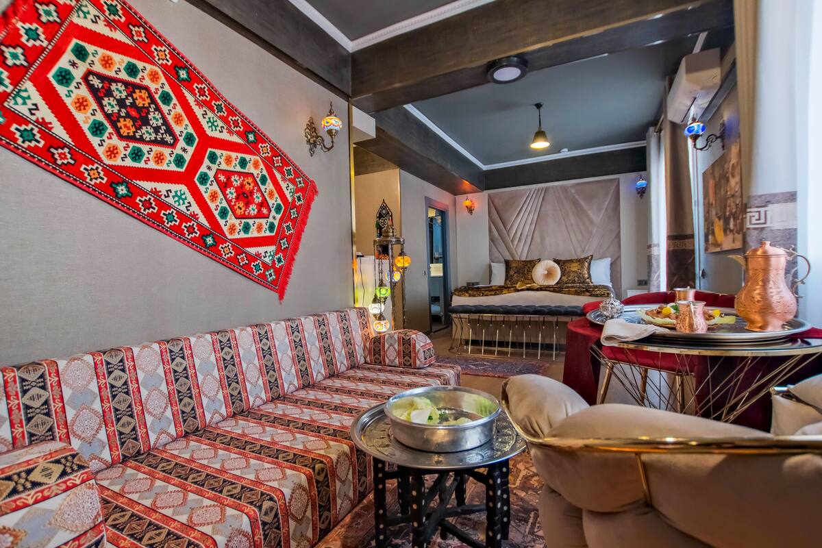 A traditional room with a patterned sofa, a dining table with a copper pot, and a decorative wall hanging.