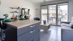 Una cocina moderna con una isla central, un área de comedor con mesa y sillas, y un balcón con vista a la ciudad.