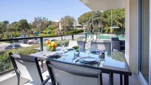 Un balcón con una mesa preparada para dos, con vista a una piscina y vegetación.