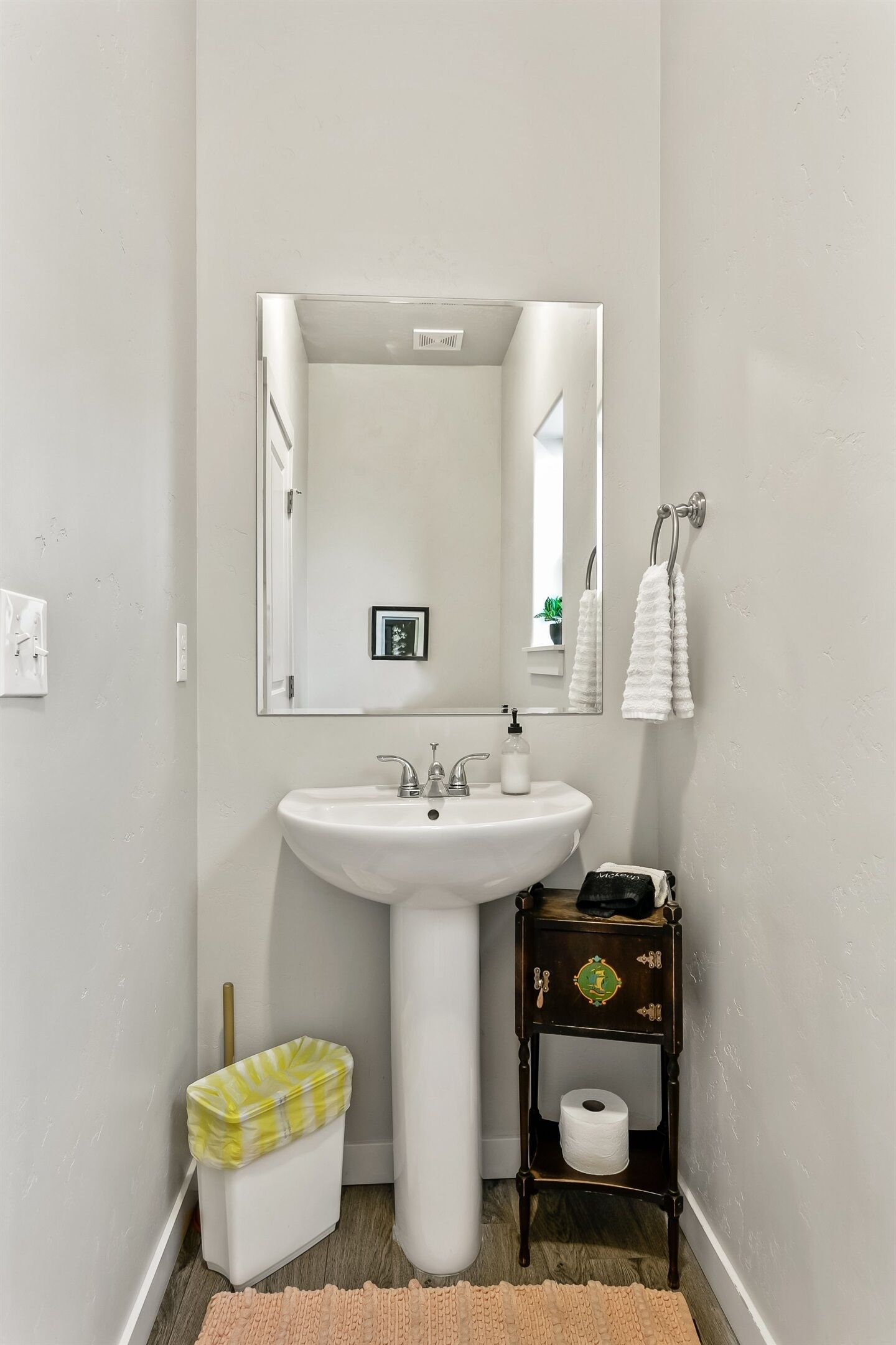 Een badkamer met een witte wastafel, spiegel en een klein houten plankje met een toiletrol.