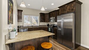 A modern kitchen with dark wood cabinets, stainless steel appliances, a granite countertop, and pendant lighting. - Perfect For Groups | Near The Village & Mall (Boise)