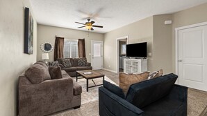 A living room with a sofa, a coffee table, a TV stand, and a ceiling fan. - Perfect For Groups | Near The Village & Mall (Boise)