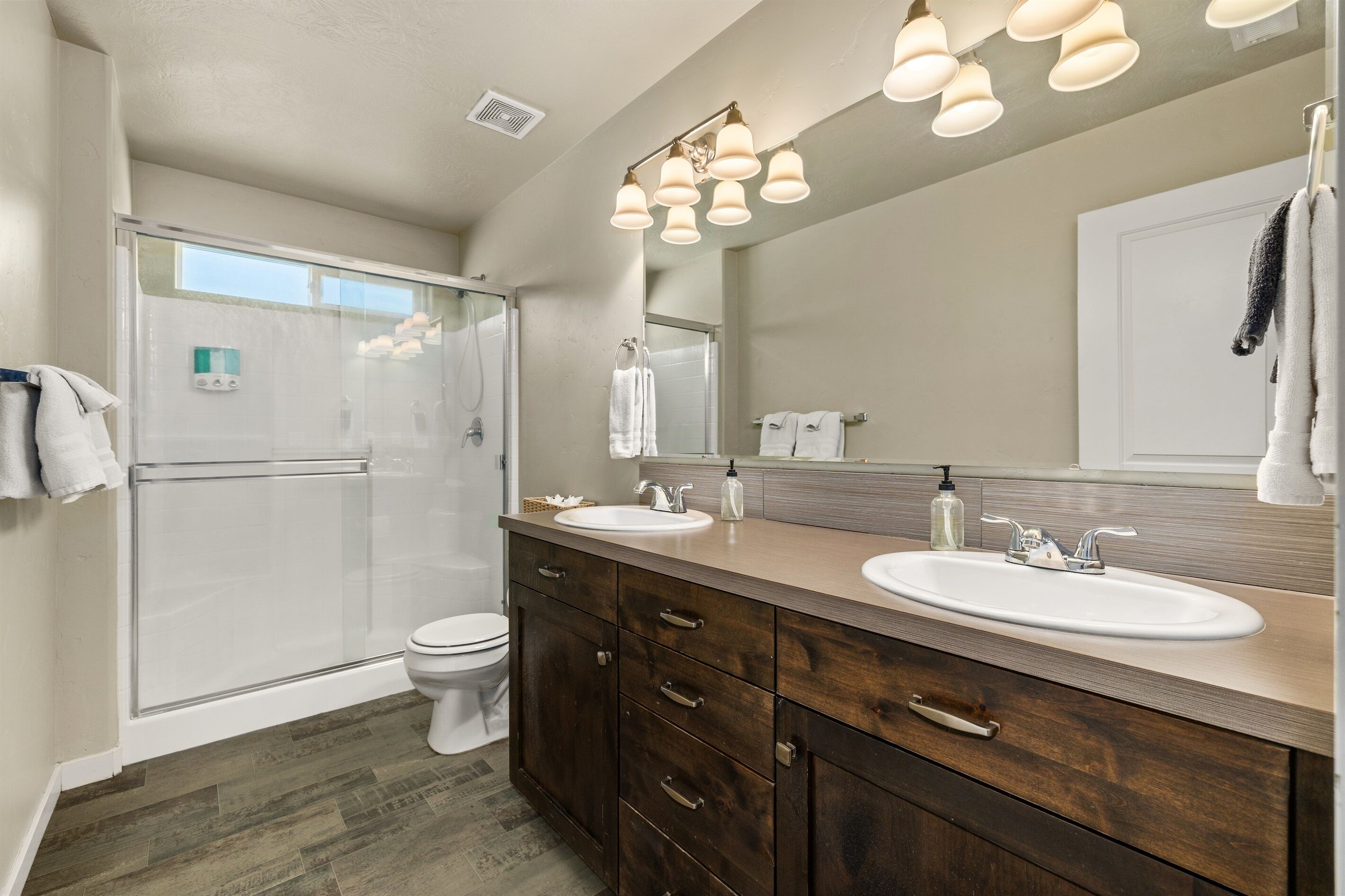 A bathroom with a glass shower enclosure, two sinks, a large mirror, and wooden cabinetry.