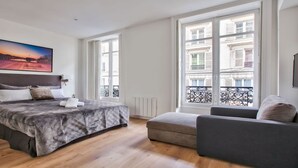 A modern bedroom with a large bed, a small sofa, and a balcony with a view of buildings. - IN AN ELEGANT SETTING AND FLOODED WITH LIGHT – CHAMPS ELYSEES -RUE JEAN MERMOZ (Paris)