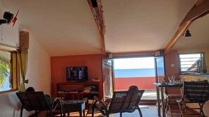 Ein Zimmer mit Fernseher, Holzmöbeln und Blick auf den Ozean.