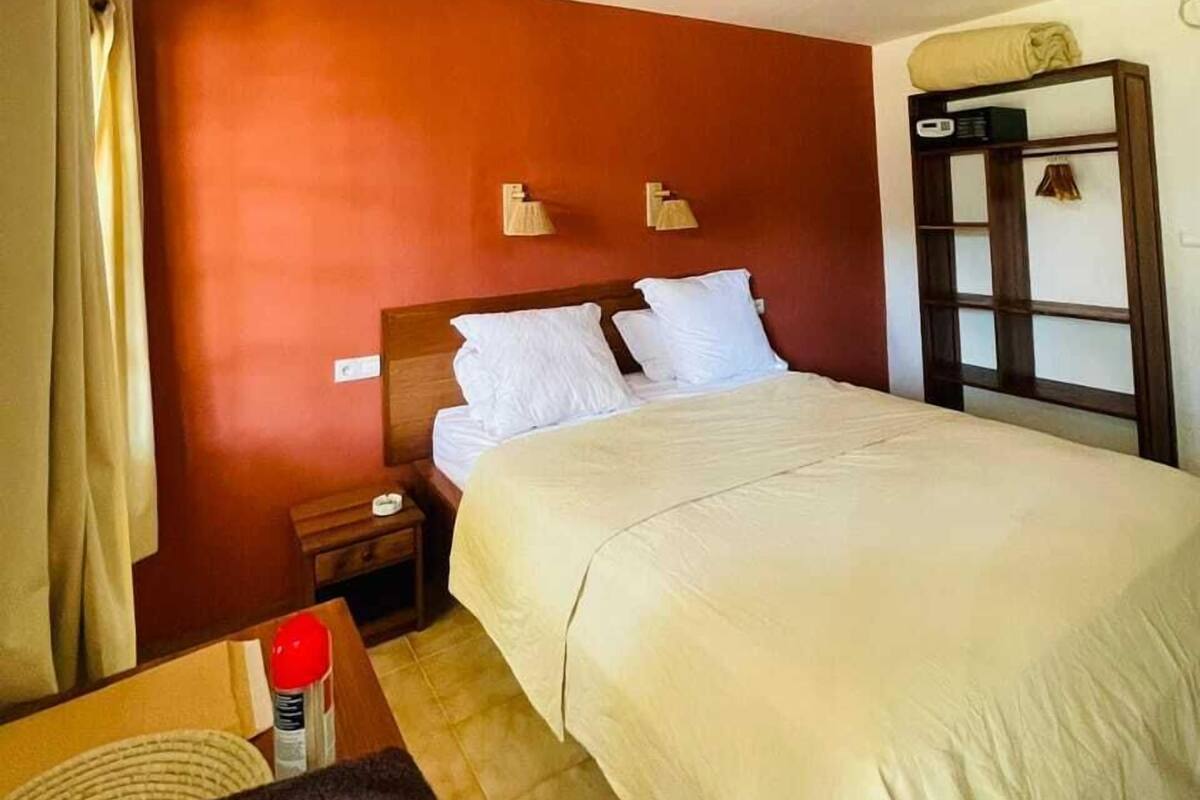 A hotel room with a large bed, a bedside table, a nightstand, and a wall-mounted shelf with a lamp.