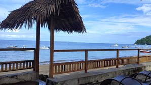 Blick auf einen Strand mit Holzgeländer, einem Reetdach und einer Reihe von Stühlen, die zum Meer hinweisen.