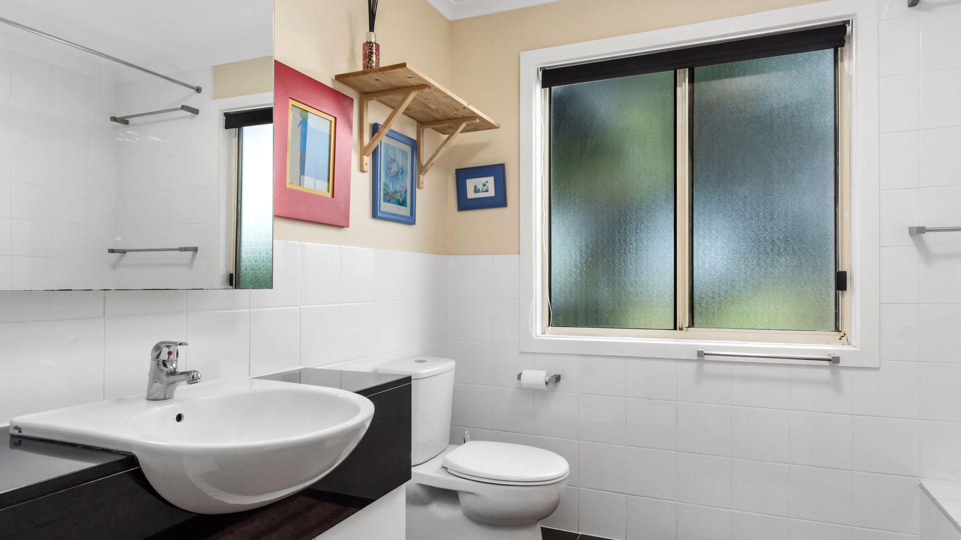 Un baño con lavamanos blanco, inodoro y ventana con vidrio esmerilado.