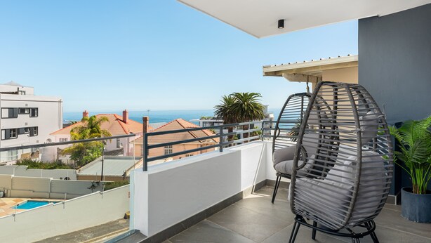 A balcony with a view of the sea, a wicker chair, and a potted plant. - 7 on Bantry 301 (Cape Town)