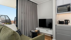 A modern living room with a flat-screen TV, a sofa, a small side table, and a kitchen area with a microwave and coffee maker. - 7 on Bantry 301 (Cape Town)