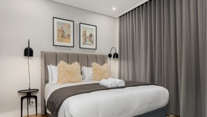 A modern bedroom with a large bed, two framed pictures on the wall, and a grey curtain. - 7 on Bantry 301 (Cape Town)