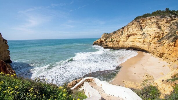 Un paysage côtier avec une plage, des falaises rocheuses et un ciel dégagé.