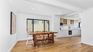 A modern kitchen with white cabinets, a wooden dining table, and a large window.