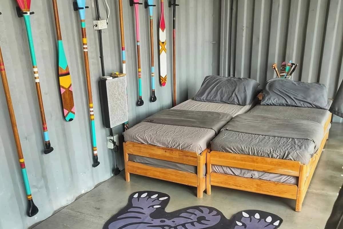 A room with a bed, a rug, and a wall displaying various wooden paddles.