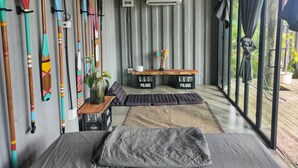 Una habitación moderna con una cama, un banco y una mesa con una planta. Hay palas de colores en la pared y un equipo de aire acondicionado.