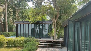 Un espacio exterior moderno con terraza de madera, plantas en macetas y una estructura de cristal.