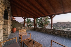 A covered outdoor seating area with stone walls, a wooden bench, and a table with a wine glass.