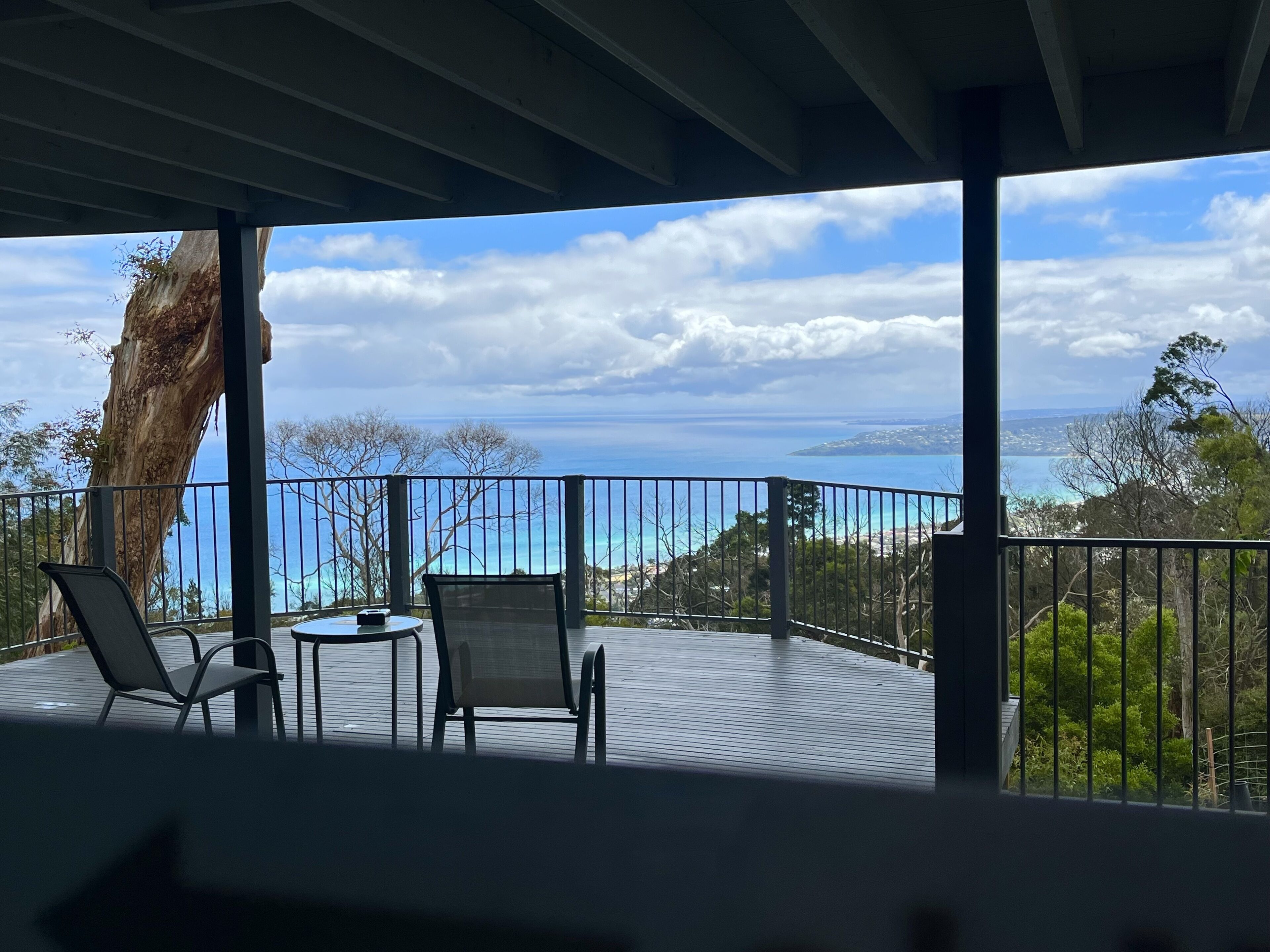A covered outdoor area with two chairs and a table, overlooking a scenic view of the ocean and distant land.
