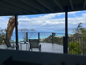 A covered outdoor area with two chairs and a table, overlooking a scenic view of the ocean and distant land. - Arthurs Holiday Villa (Arthurs Seat)